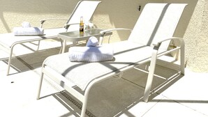 A sunlit outdoor seating area with two white lounge chairs, a small table, and a bottle of Corona beer. - Pool Home with Spa in Gated Resort Community with Game Room (Kissimmee)
