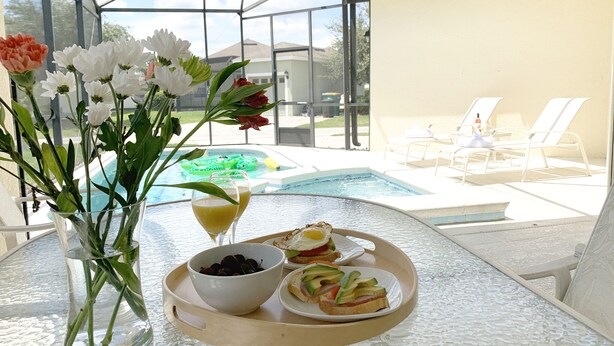 A glass table with a tray containing food, a glass of juice, and a bowl of berries. - Pool Home with Spa in Gated Resort Community with Game Room (Kissimmee)