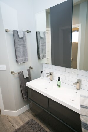 A bathroom with a white vanity, two towel racks with towels, a large mirror, and a bottle of soap. - Downtown Mountain Views Craftsman Stunner 5 bd/4b (Fort Collins)