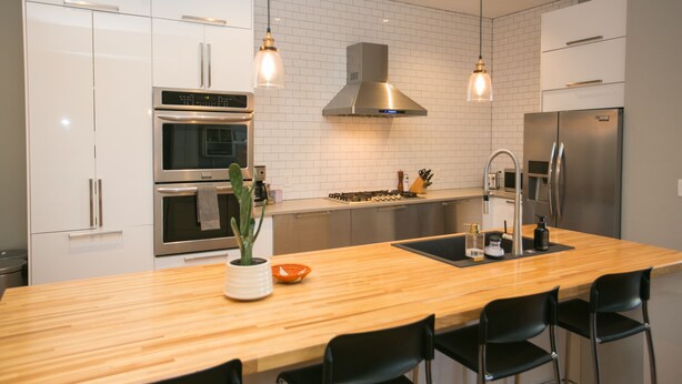 A modern kitchen with white cabinets, stainless steel appliances, a wooden island, and pendant lighting. - Downtown Mountain Views Craftsman Stunner 5 bd/4b (Fort Collins)