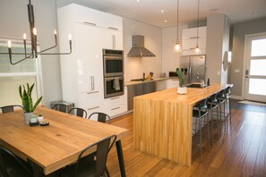 A modern kitchen with white cabinetry, a wooden island, stainless steel appliances, and pendant lighting. - Downtown Mountain Views Craftsman Stunner 5 bd/4b (Fort Collins)