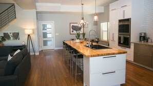 A modern kitchen with a central island, stainless steel appliances, and a dining area with a sofa and chairs. - Downtown Mountain Views Craftsman Stunner 5 bd/4b (Fort Collins)