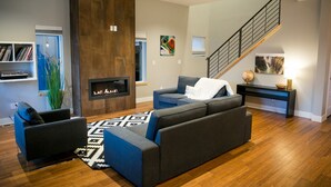 A modern living room with a fireplace, a staircase, and a bookshelf. - Downtown Mountain Views Craftsman Stunner 5 bd/4b (Fort Collins)