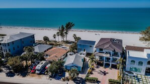 A coastal hotel with multiple buildings, a beach, and parked vehicles.