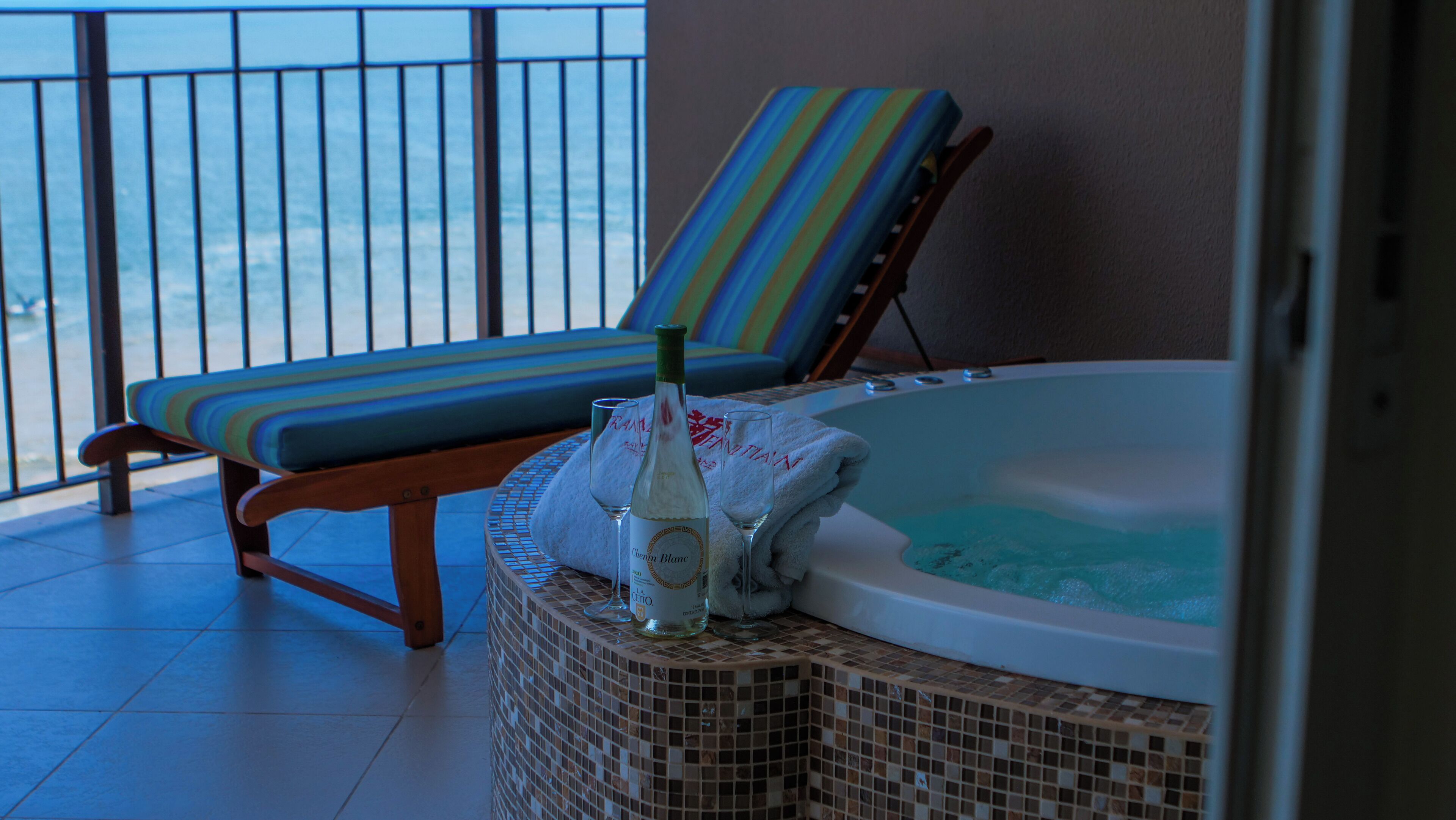 Un fauteuil de relaxation et un jacuzzi, avec une bouteille de champagne et des verres, sur une plateforme carrelée.