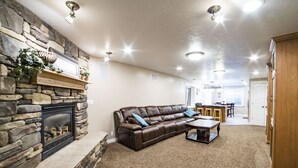 A living room with a stone fireplace, a brown leather sofa, a wooden coffee table, and a kitchen area in the background.