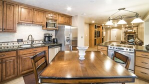 A kitchen with wooden cabinets, a stainless steel refrigerator, a microwave, a coffee maker, and a dining table with chairs.