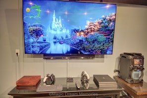Enjoy entertainment at its finest with a TV featuring a scenic castle view, a gaming console, and a glass table with a keyboard and mouse.