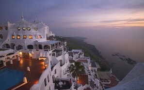 A resort with multiple white buildings, a swimming pool, and a view of the coastline.