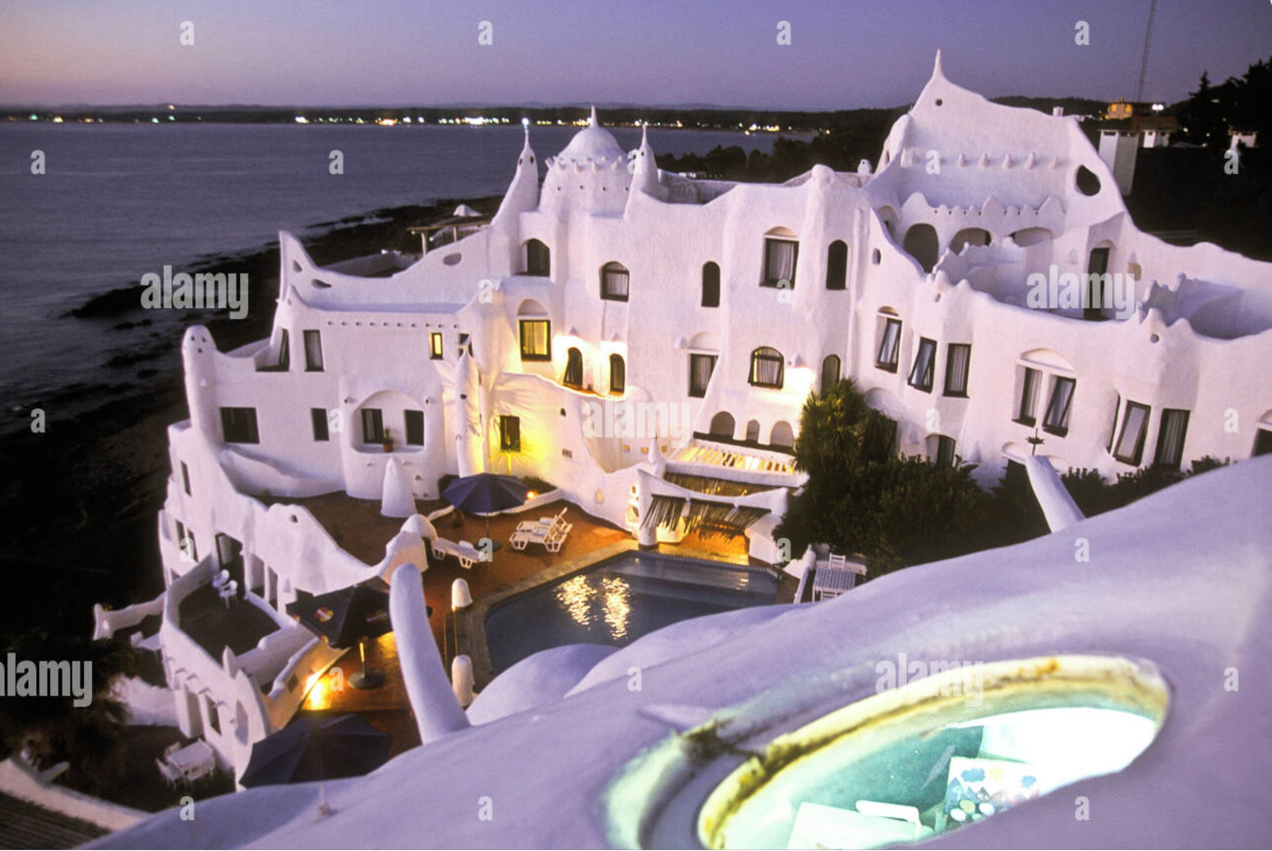 Un edificio blanco con numerosas ventanas y balcones, una piscina y vista al mar.