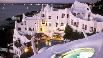 Un edificio blanco con numerosas ventanas y balcones, una piscina y vista al mar.