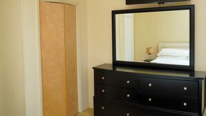 A bedroom with a ceiling fan, a large mirror, a TV mounted above the mirror, a wooden door, and a black dresser with drawers.