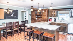 A kitchen with a central island, wooden chairs, pendant lights, and a chalkboard sign. - Large beautiful house on lake. Dock, Water trampoline, Fire Pit, Rope Swing, 4/3 (Lake Placid)