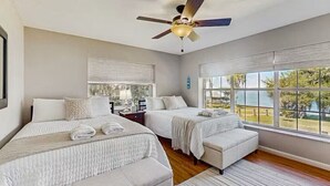 A bedroom with two beds, a ceiling fan, and large windows offering a view of the outdoors. - Large beautiful house on lake. Dock, Water trampoline, Fire Pit, Rope Swing, 4/3 (Lake Placid)