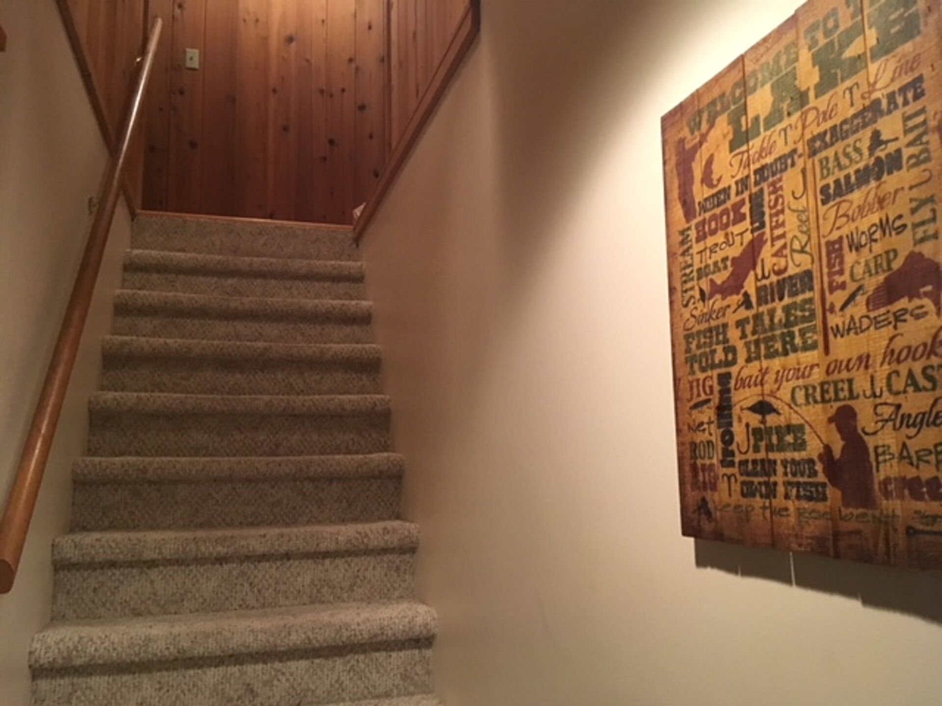 Una escalera con alfombra, barandillas de madera y una pared con varias palabras y frases relacionadas con la pesca.