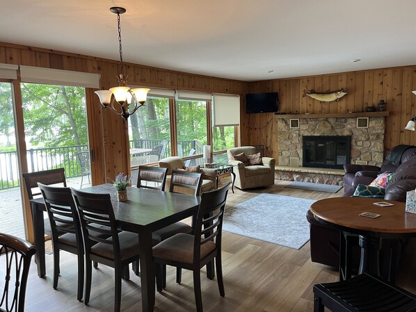 A cozy cabin interior with a dining area, a fireplace, and a balcony with a view of trees.