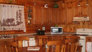 A wooden kitchen with a dining table and chairs, a microwave, a stove, and various kitchen cabinets. - Bears Den on the private lake (Winter)