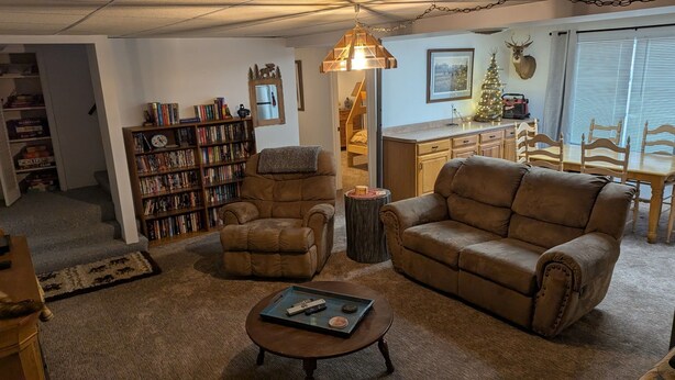 A cozy living room with a fireplace, a bookshelf, a dining area with wooden furniture, and a Christmas tree. - Bears Den on the private lake (Winter)
