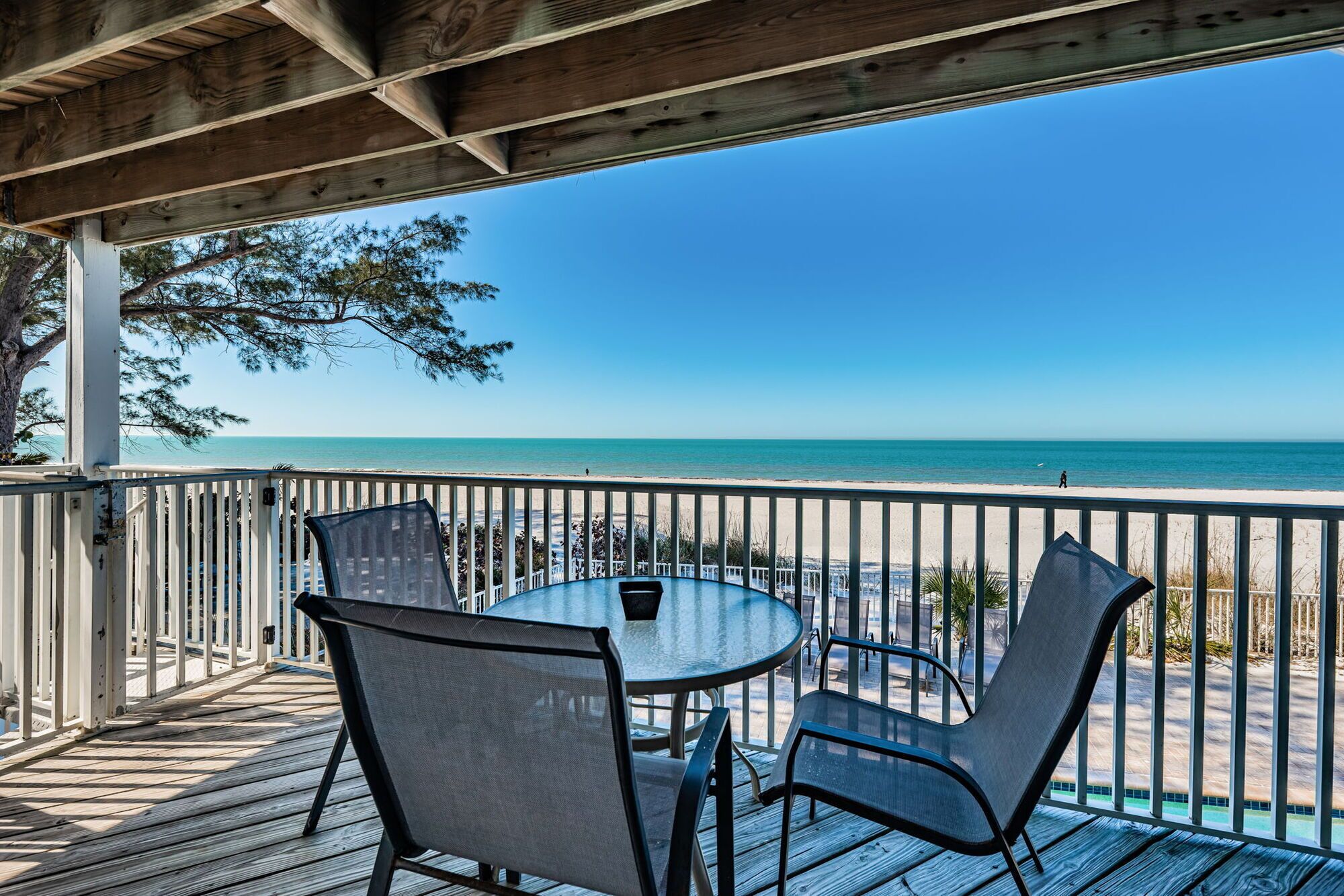 A covered outdoor seating area with a table and chairs, overlooking a beach.