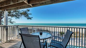 A covered outdoor seating area with a table and chairs, overlooking a beach.