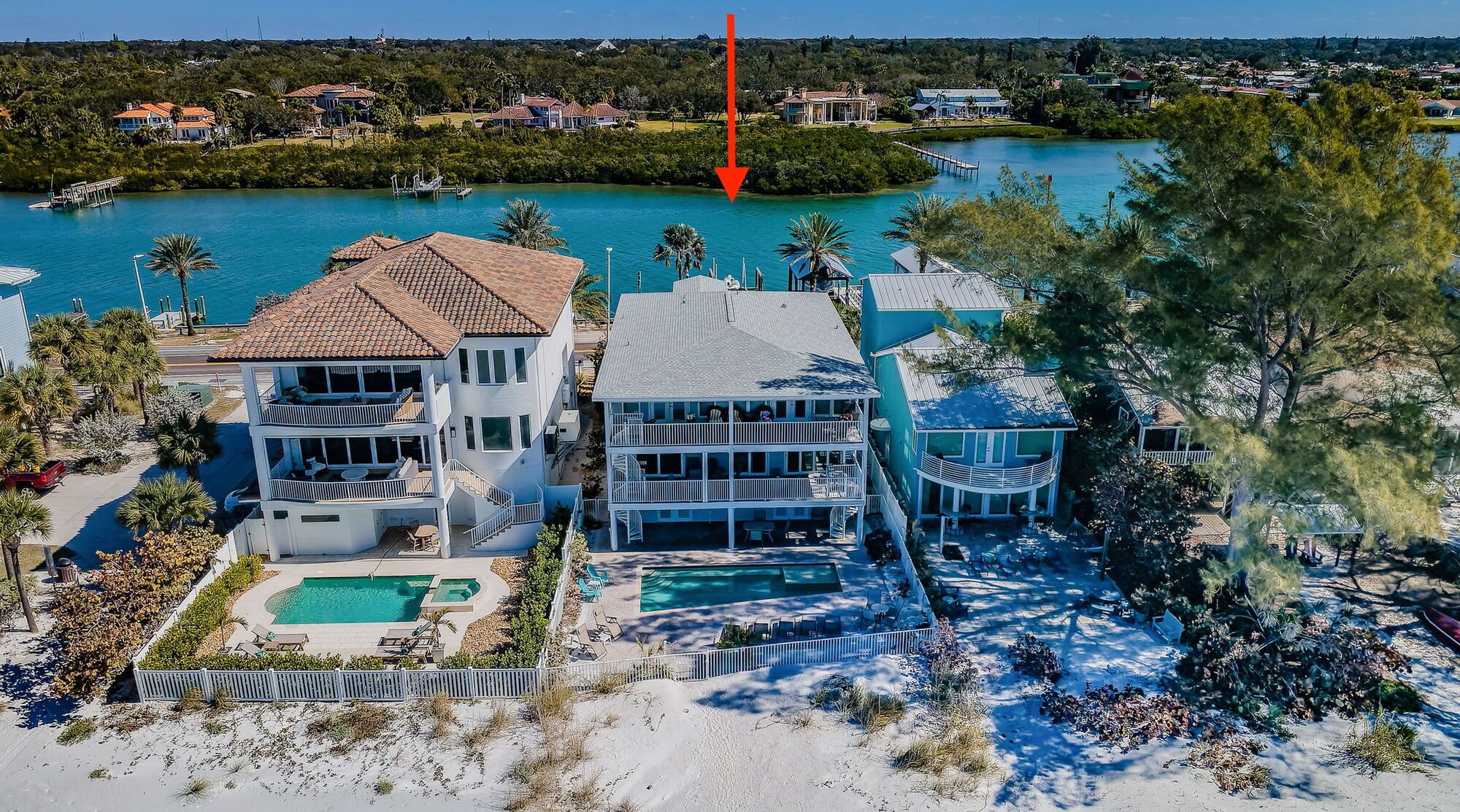 A beachfront property with a large house, a pool, and a view of the ocean.