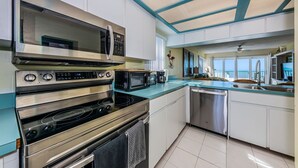 Una cocina moderna con electrodomésticos de acero inoxidable, una encimera verde azulada y vistas al océano a través de amplias ventanas.