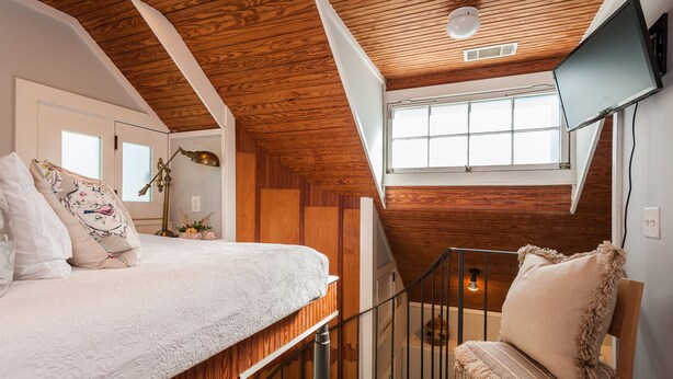 A bedroom with a lofted sleeping area, wooden ceiling, a TV mounted on the wall, and a window providing natural light. - Carriage House, Forsyth Park, Pet friendly, private courtyard 🩷 (Savannah)