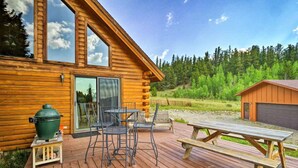 Una cabaña de madera con terraza, una parrilla y una mesa de picnic.