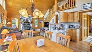 Interior acogedor de una cabaña con comedor, cocina y chimenea de piedra.
