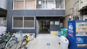 A building with a two-story entrance, a vending machine, and bicycles parked outside. - Best Residence Kujo 502 (Osaka)
