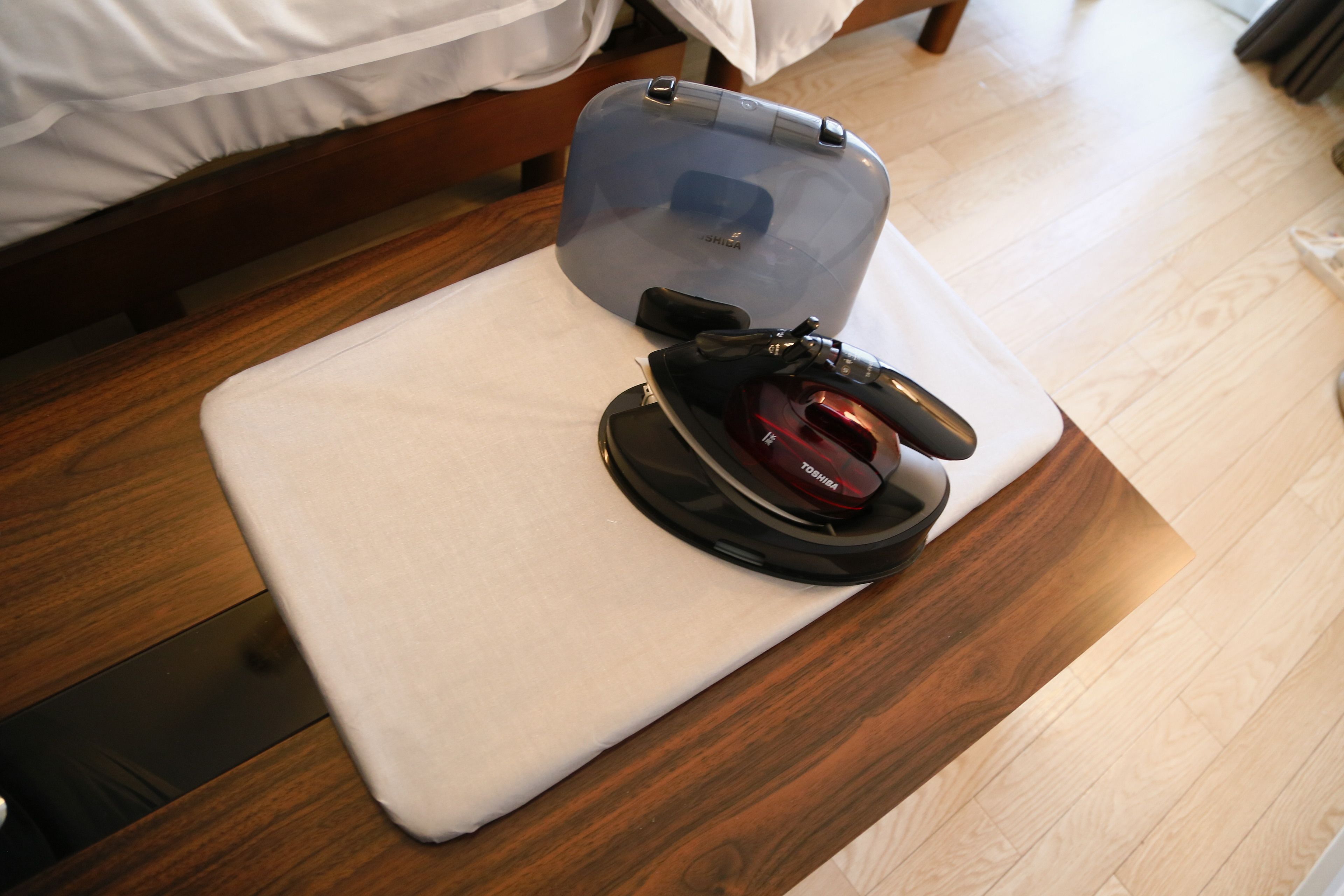 A compact iron and a portable iron on a bedside table in a hotel room.