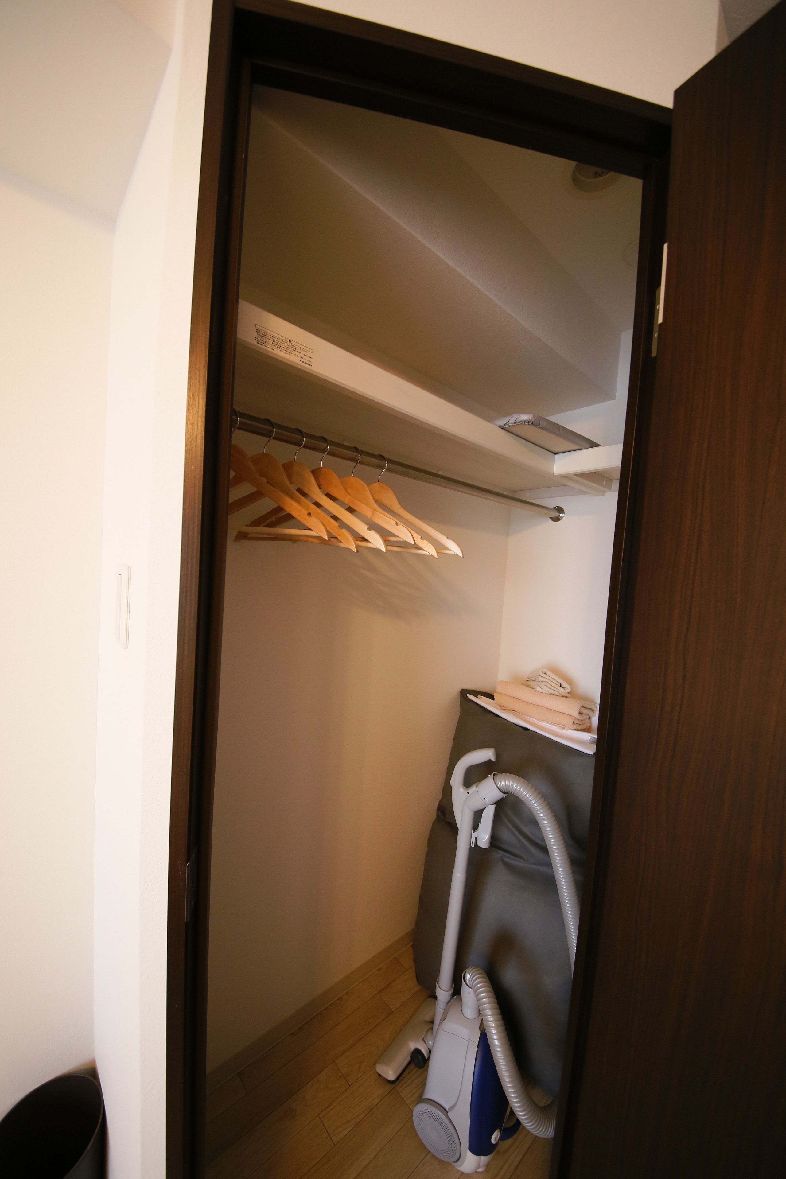 A small, compact closet with a vacuum cleaner and a shelf with folded clothes.