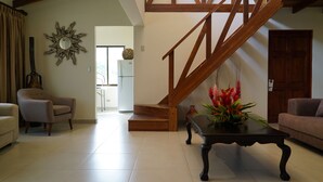 A spacious living room with a wooden staircase, a dining area, and a kitchen in the background. - Sunset del Mar Beach Front House (Parrita)
