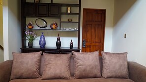 A living room with a brown sofa, a dark wooden cabinet with decorative items, and a wooden door. - Sunset del Mar Beach Front House (Parrita)