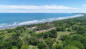 An aerial view of a coastal property with a beach, dense greenery, and a clear sky. - Sunset del Mar Beach Front House (Parrita)