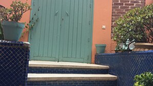A set of concrete steps leading to a green door with a metal handle, flanked by potted plants and a blue-tiled wall. - El Hamra Hotel (Marrakech)
