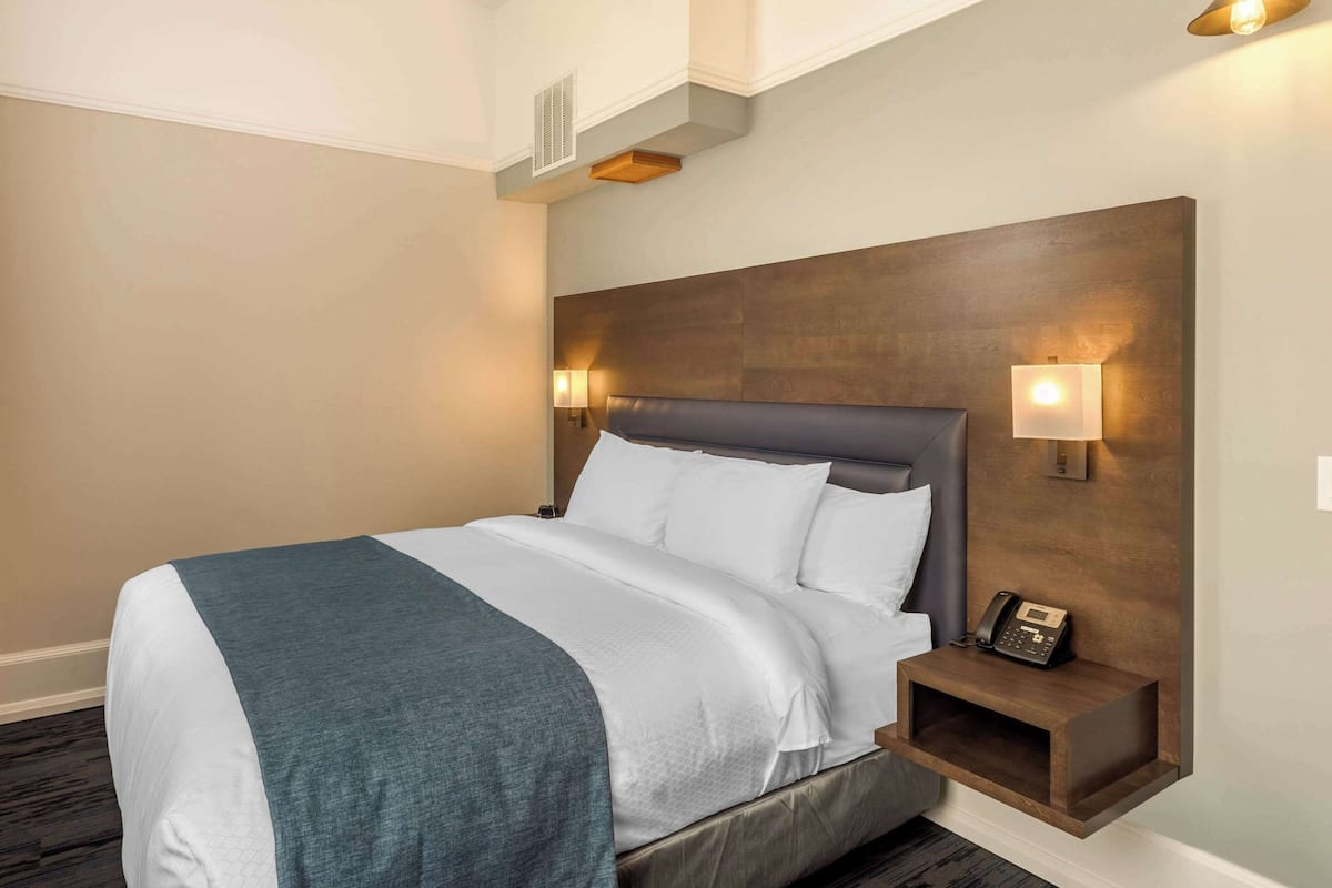 A hotel room with a large bed, a nightstand with a phone, and wall-mounted lights.