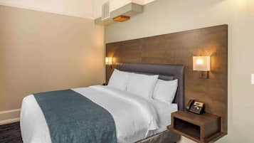 A hotel room with a large bed, a nightstand with a phone, and wall-mounted lights.