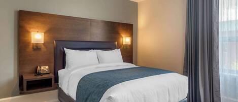 A hotel room with a large bed, two bedside lamps, a nightstand with a phone, and a window with curtains.
