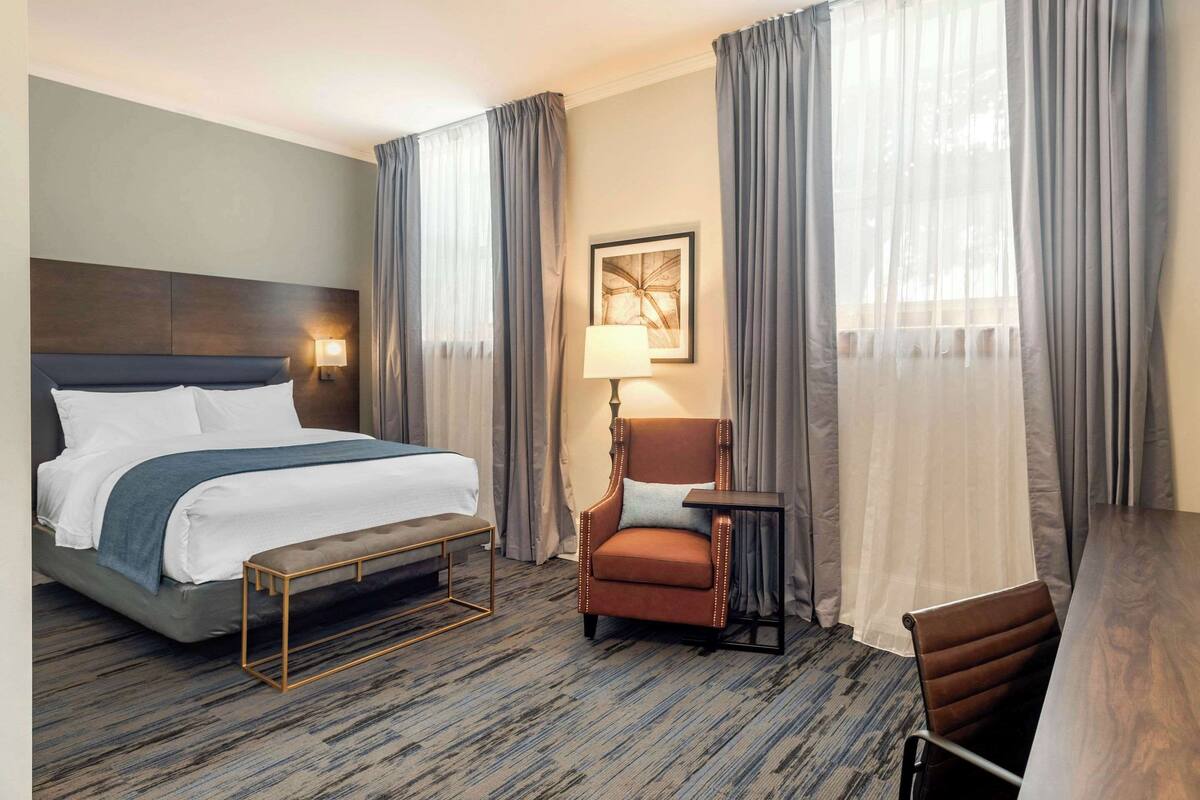 A hotel room with a bed, a desk, a chair, and a lamp.