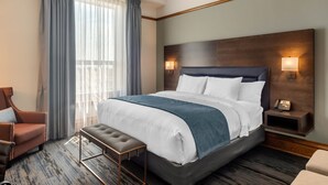 A hotel room with a large bed, a chair, a bench, a nightstand with a phone, and a window with curtains. - The Courthouse Hotel, an Ascend Collection Hotel (Thunder Bay)