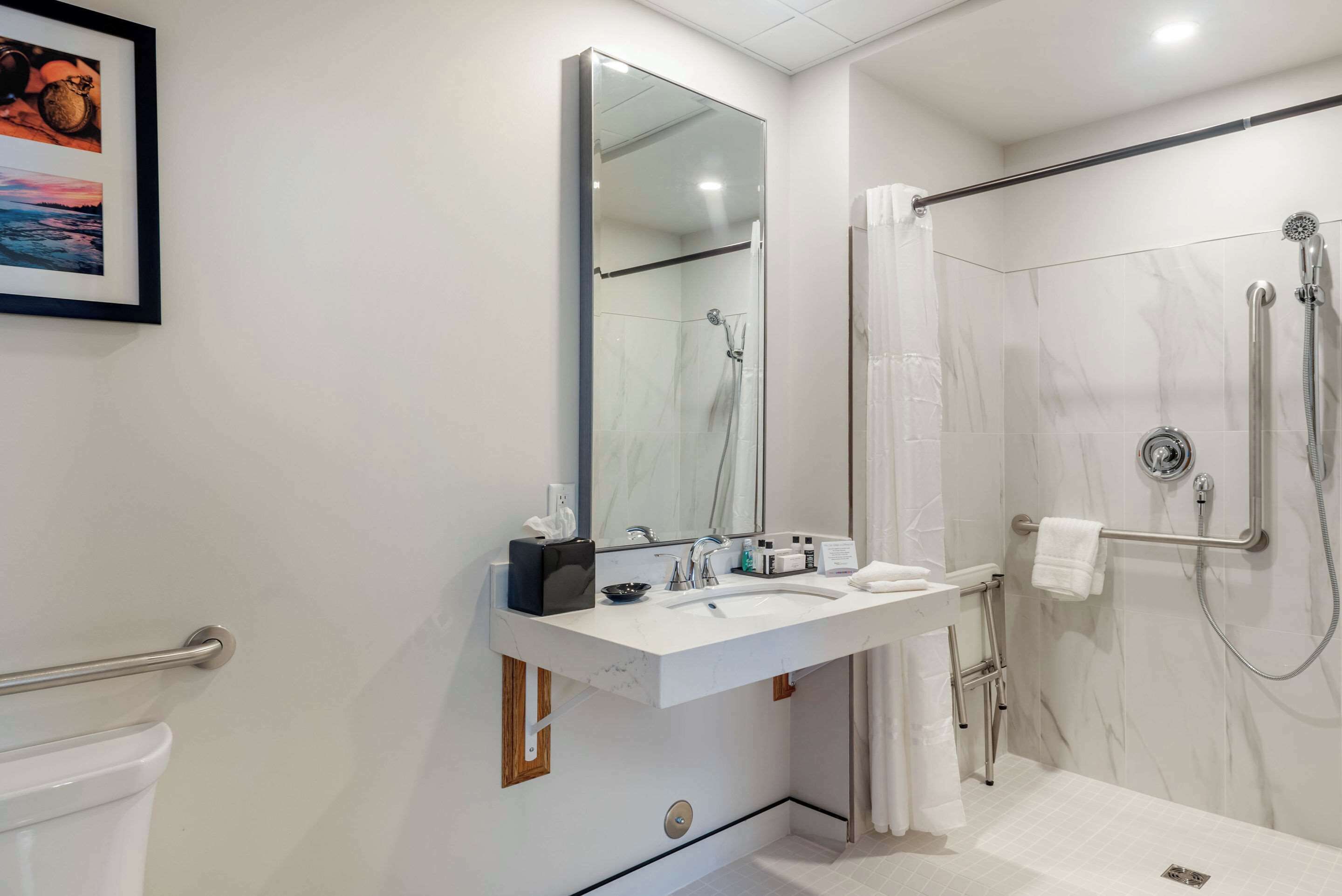 A modern bathroom with a white vanity, a large mirror, a shower with a glass door, and a towel rack.