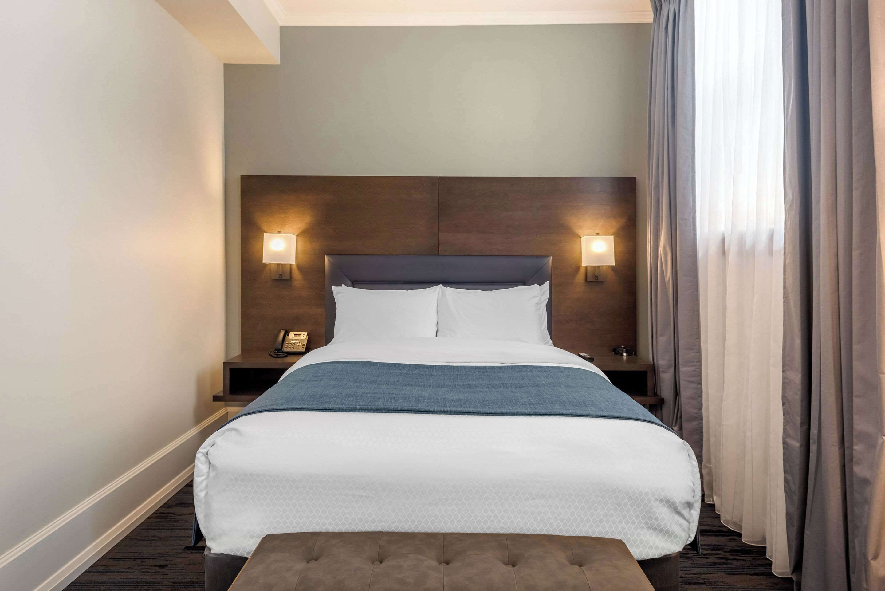 A hotel room with a large bed, two bedside lamps, a nightstand, and a window with curtains.
