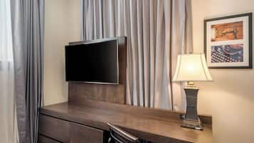 Habitación de hotel con un escritorio de madera, un televisor de pantalla plana, una lámpara y un cuadro en la pared.