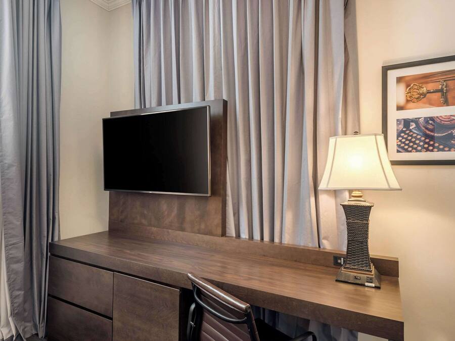 Habitación de hotel con un escritorio de madera, un televisor de pantalla plana, una lámpara y un cuadro en la pared.