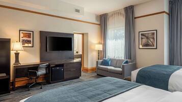 Habitación de hotel con una cama grande, un escritorio con silla, televisión, sofá y ventana con cortinas.