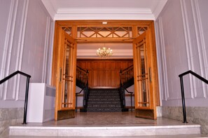 A grand entrance with a wooden staircase, a chandelier, and a white air conditioning unit. - The Courthouse Hotel, an Ascend Collection Hotel (Thunder Bay)