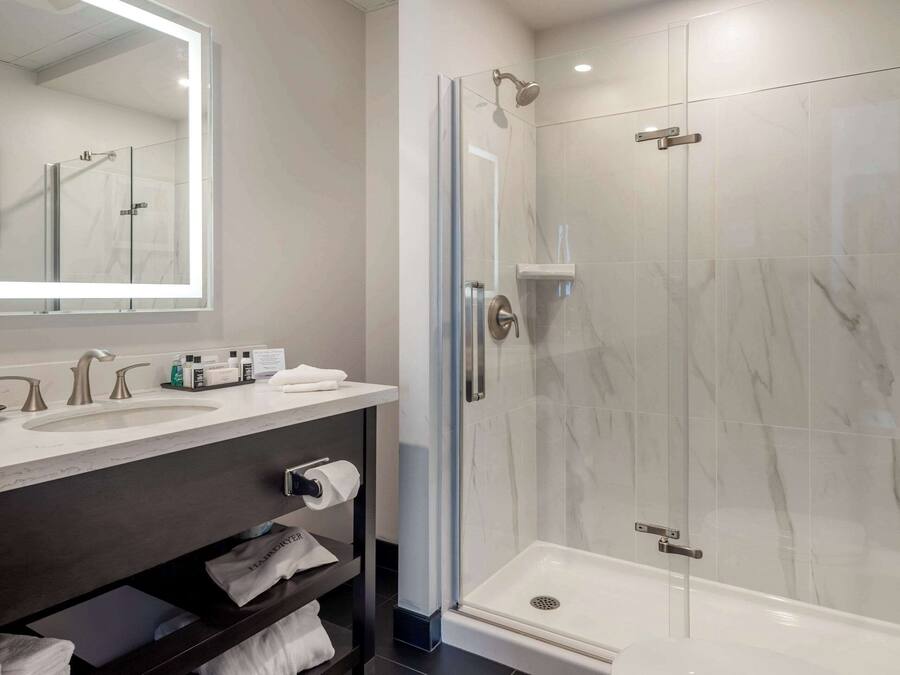 A modern bathroom with a glass-enclosed shower, a large mirror, and a vanity with a sink and towel rack.