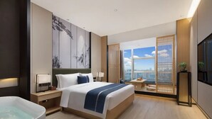 A modern hotel room with a large bed, a bathtub, a city view through floor-to-ceiling windows, and a large artwork on the wall. - Ramada by Wyndham Changsha Downtown (Changsha)