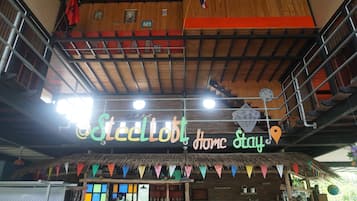 A hotel with a wooden interior, a sign reading "SteelLoft Home Stay", and colorful flags.
